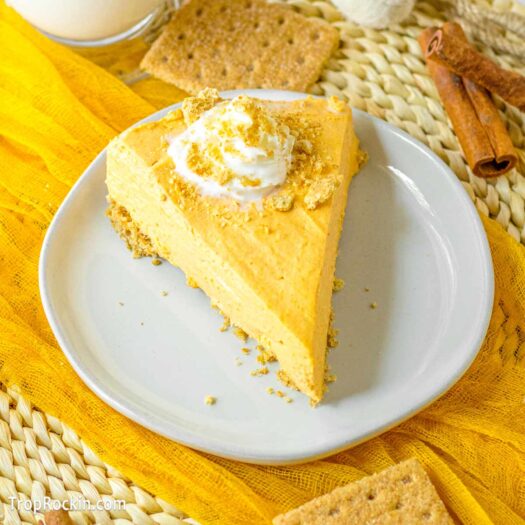 No bake pumpkin cheesecake slice topped with whipped cream on a white plate.
