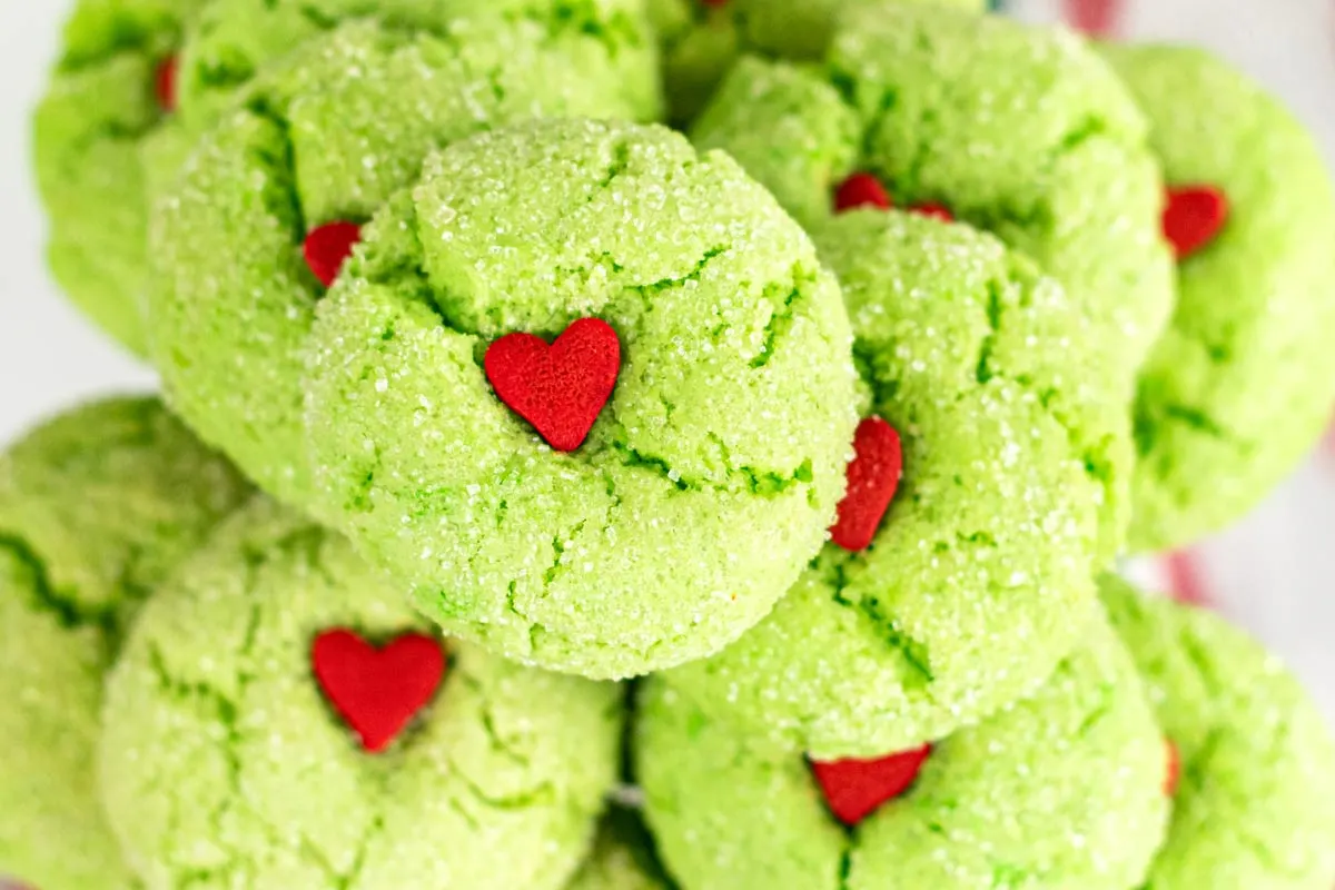 Stack of green grinch crinkle cookies with red heart sprinkles.