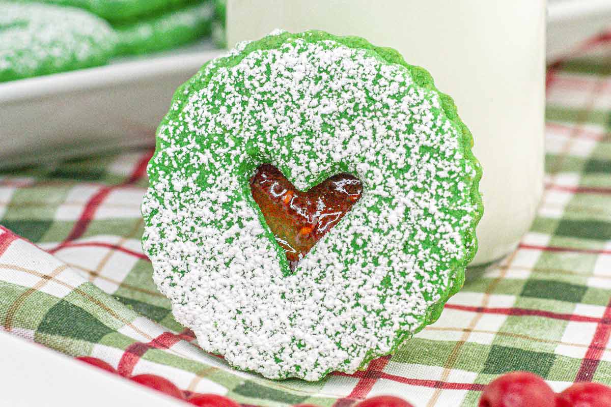 Green Grinch Linzer Cookie with a heart cutout with jam showing though the top cookie.