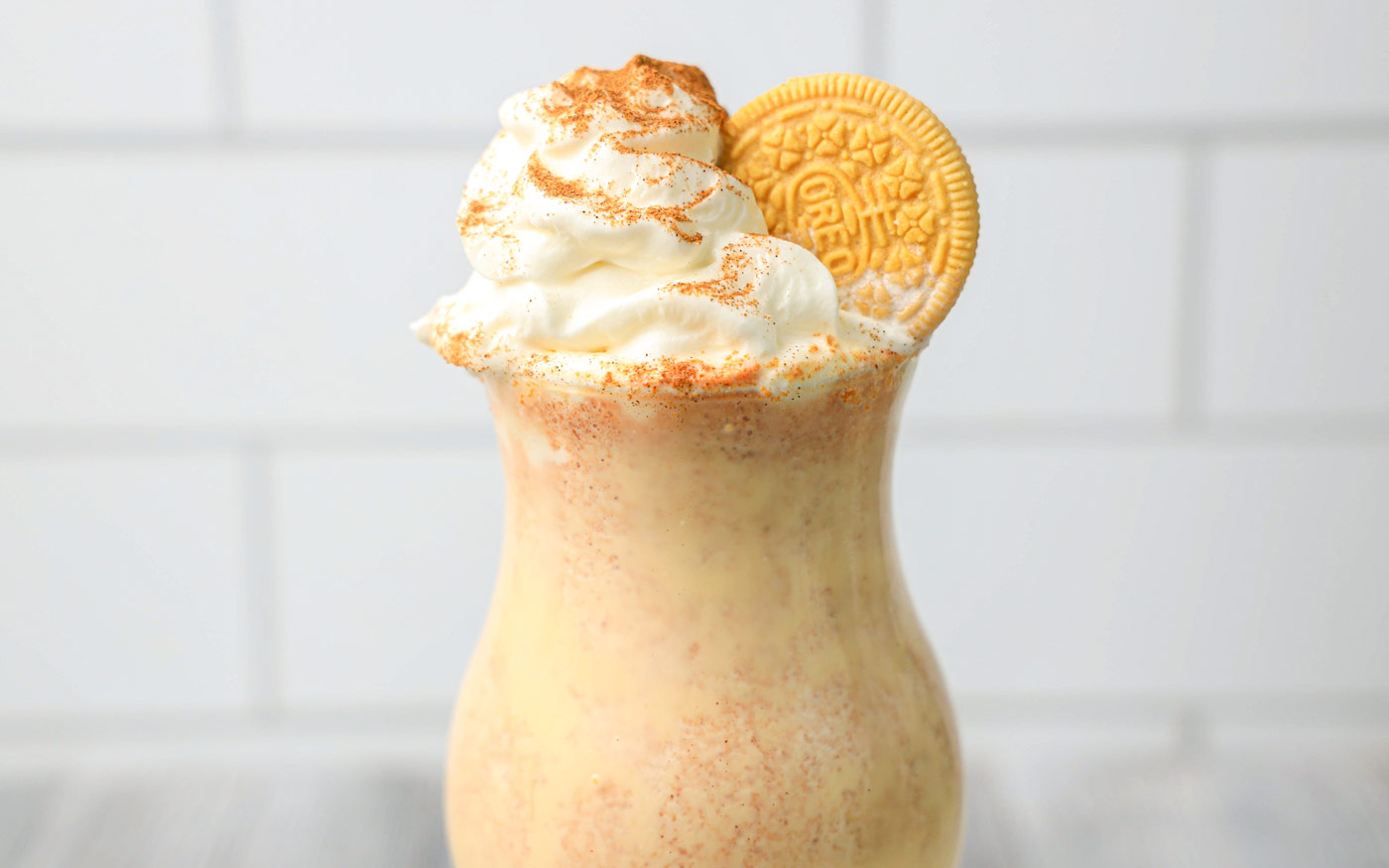 Pumpkin spice milkshake in a tulip glass with a pumpkin spice oreo and whipped cream on top and garnished with cinnamon and pumpkin spice.