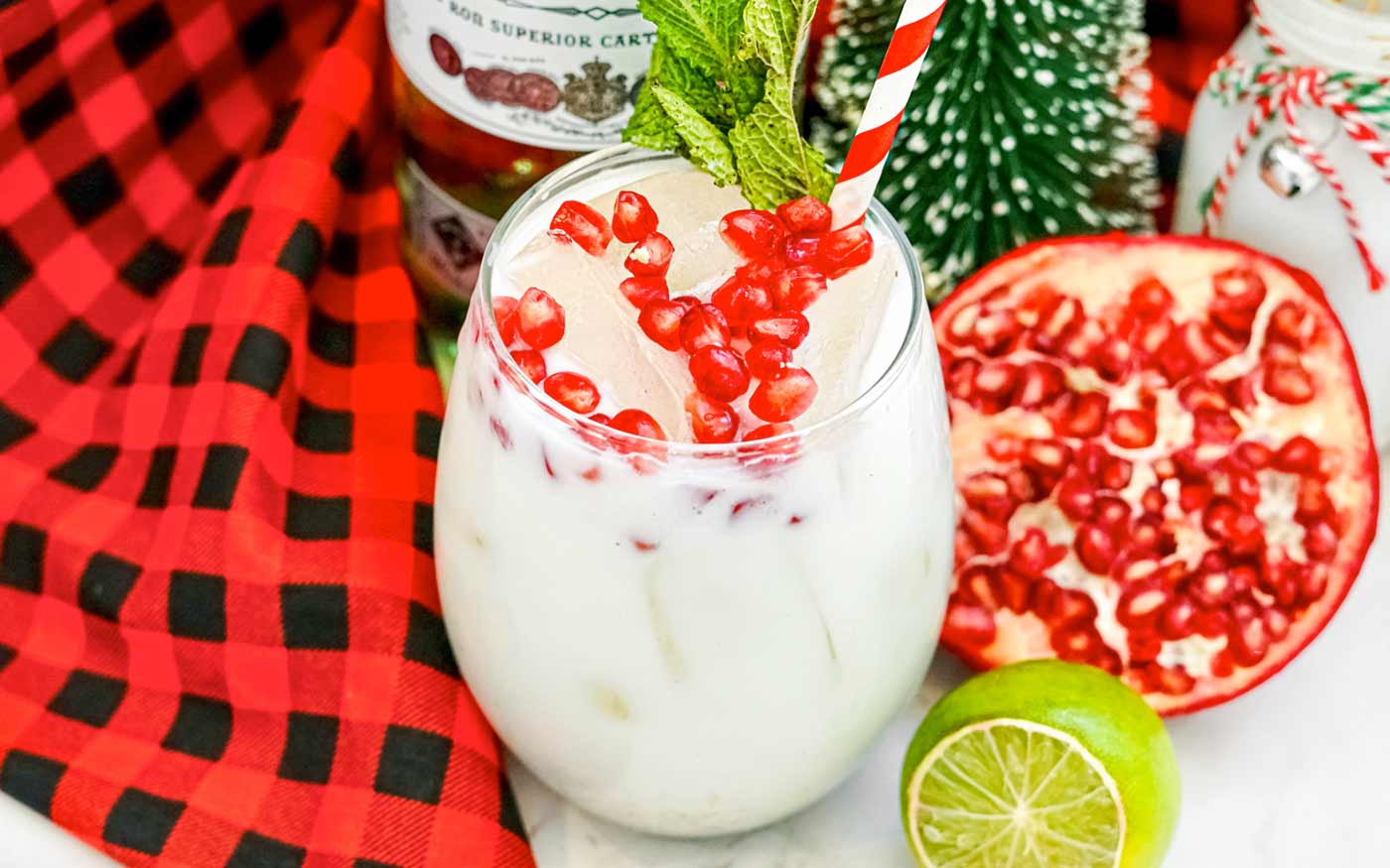 White Christmas Mojito with pomegranate arils and a mint sprig for garnish. A fresh cut pomegranate and lime in the background.