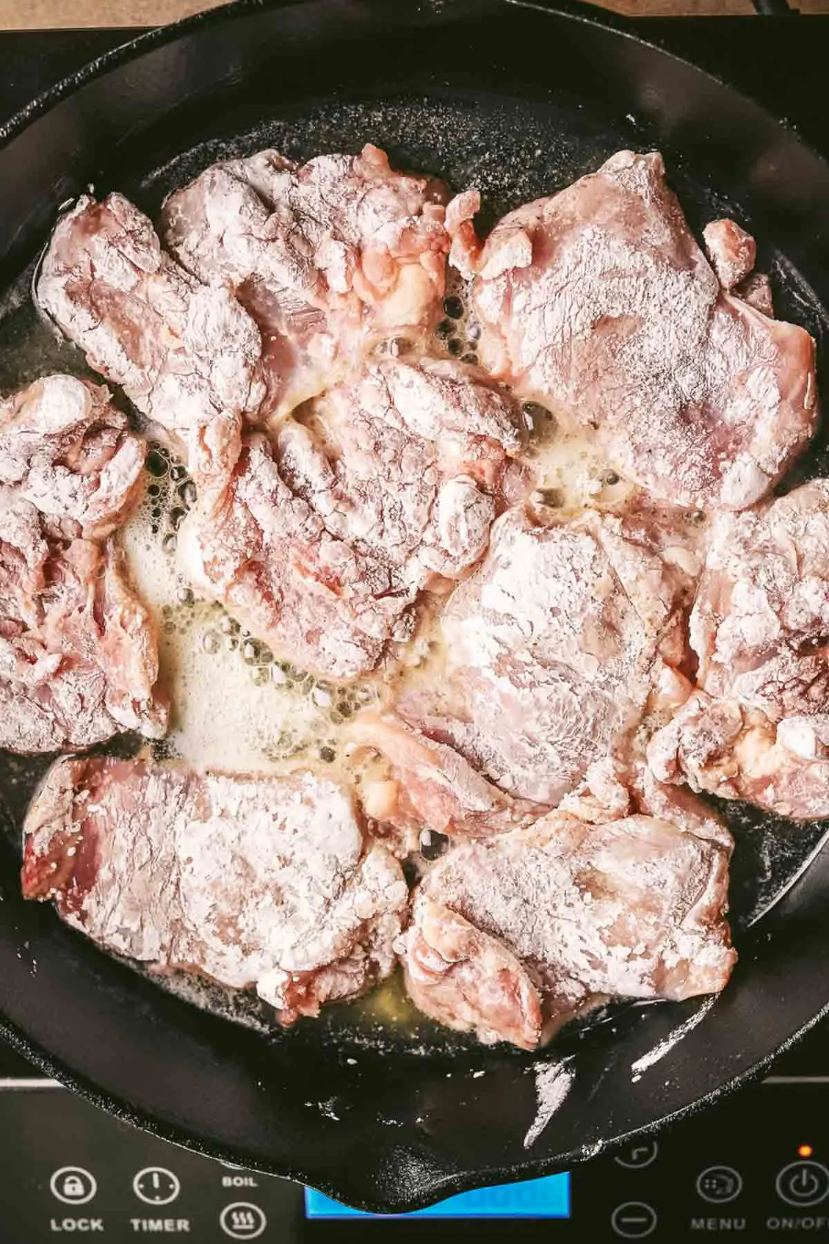 Coated chicken thighs in a skillet with hot butter and oil.
