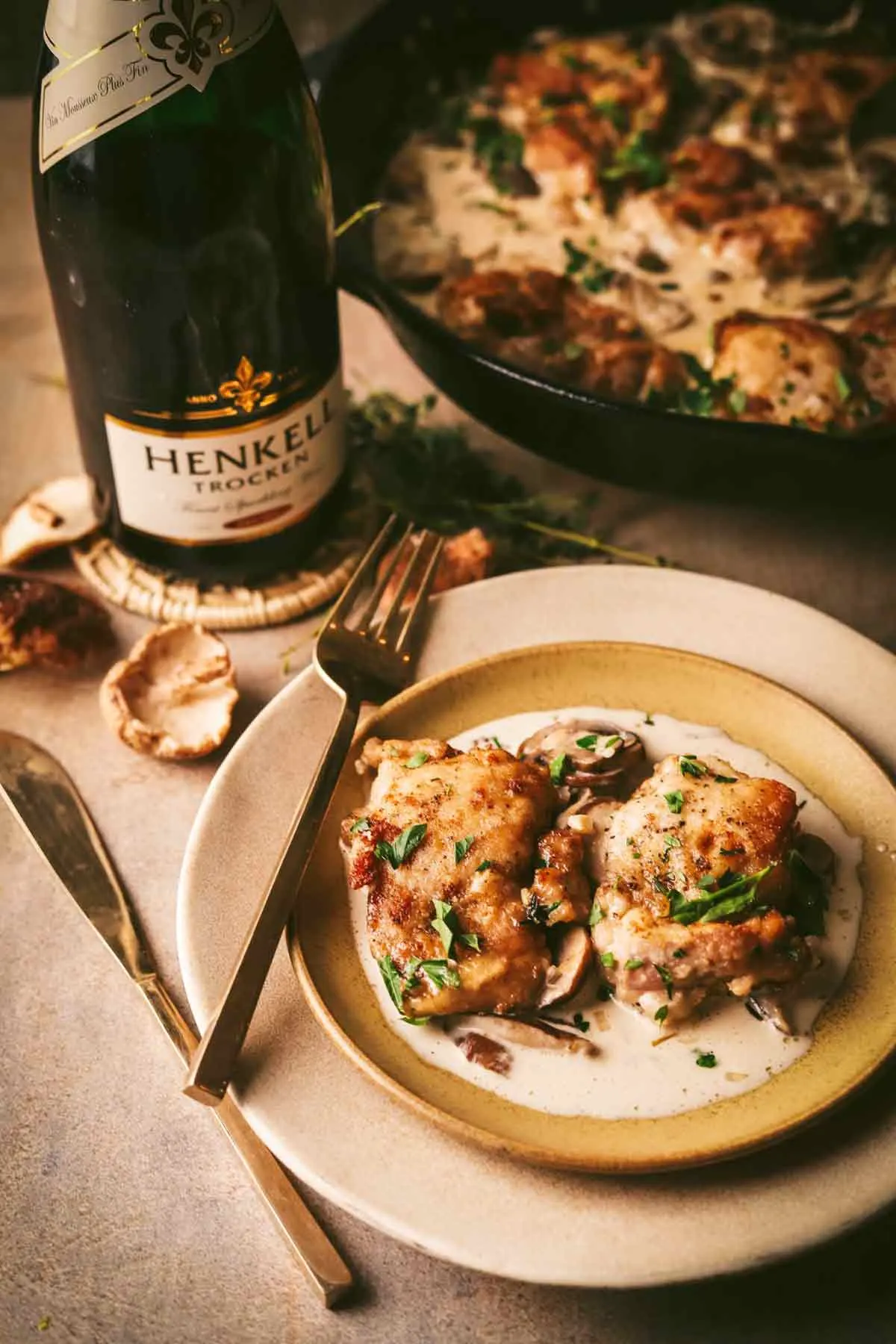 wo champagne chicken thighs on a plate with cream sauce. bottle of champagne in the background.