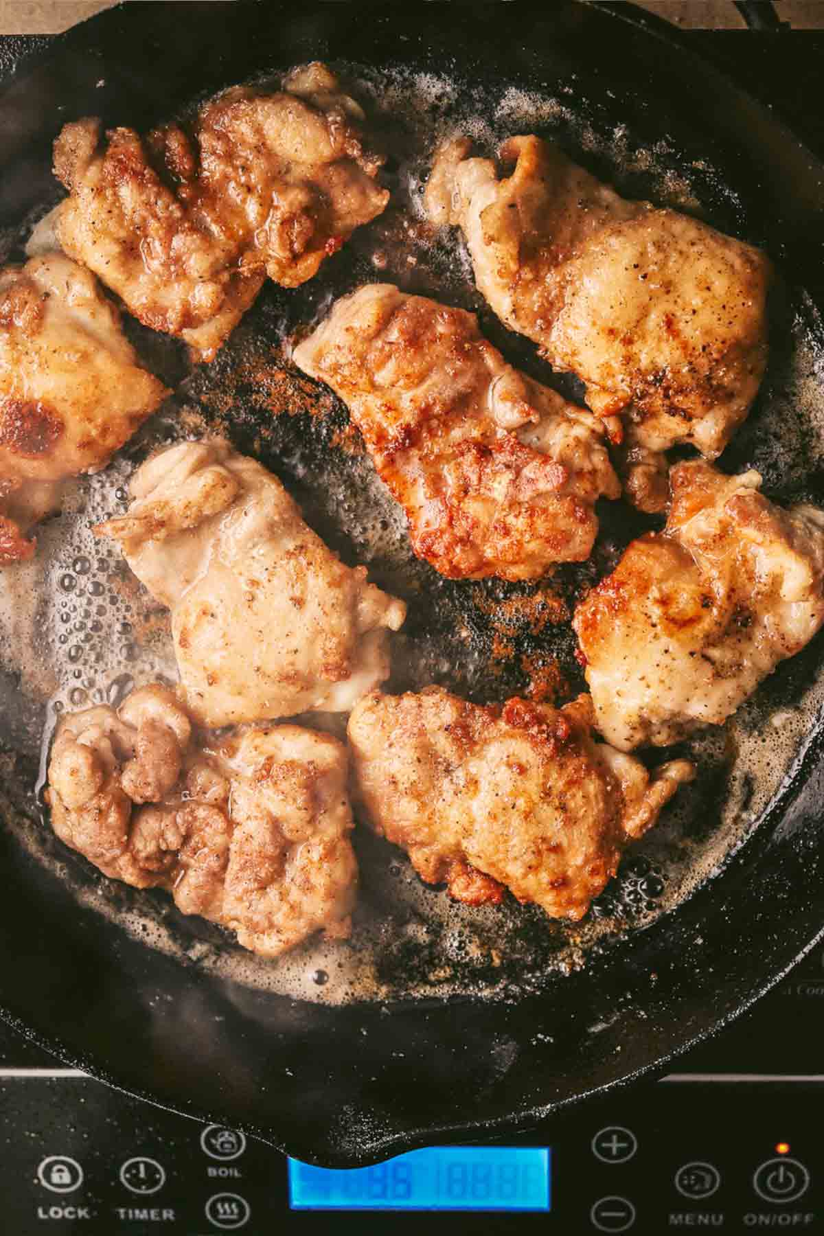 chicken thighs fried in a skillet with hot butter and oil.