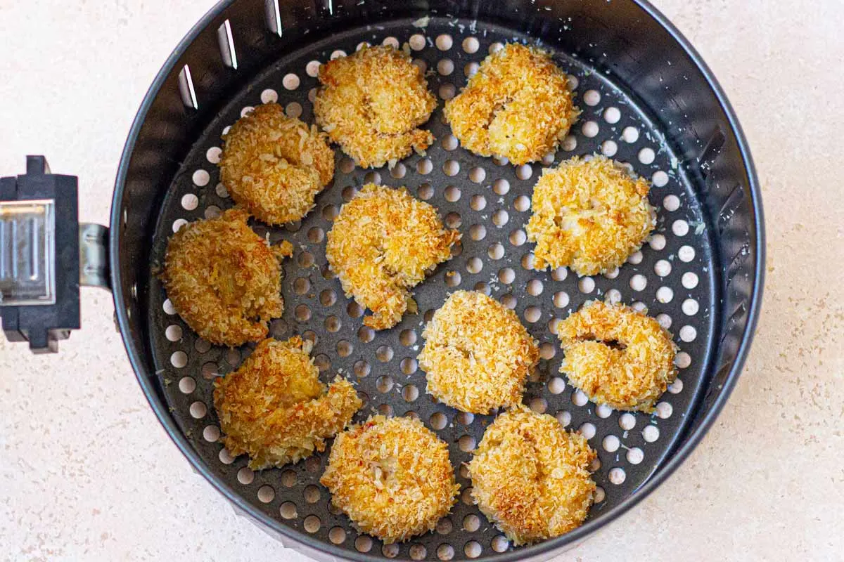 Coconut shrimp in the air fryer basket spaced evenly in a single layer.