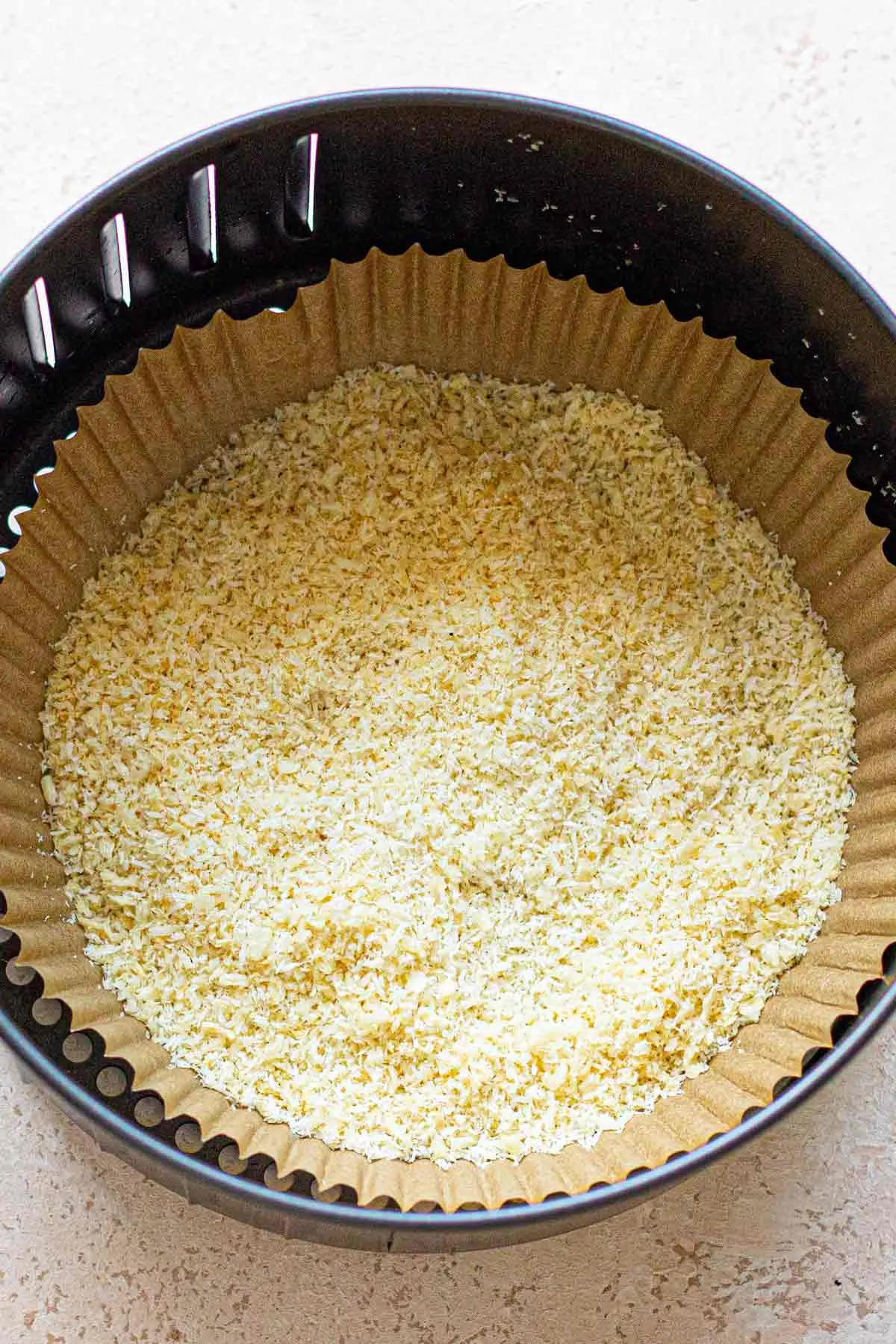 Breadcrumbs and coconut flakes in air fryer basket with an air fryer parchment paper lining,
