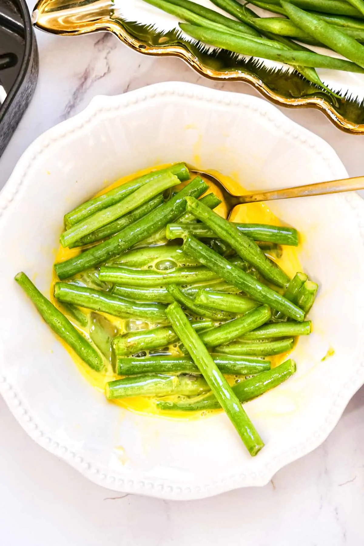 Raw green beans in a bowl of whisked eggs.