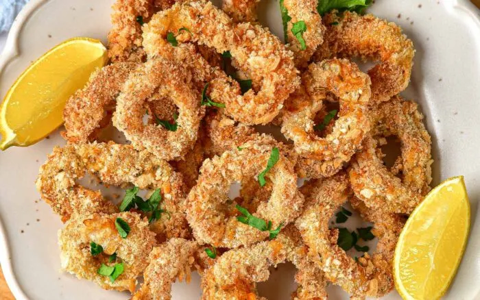 air fryer calamari stacked on a plate with two lemon wedges.