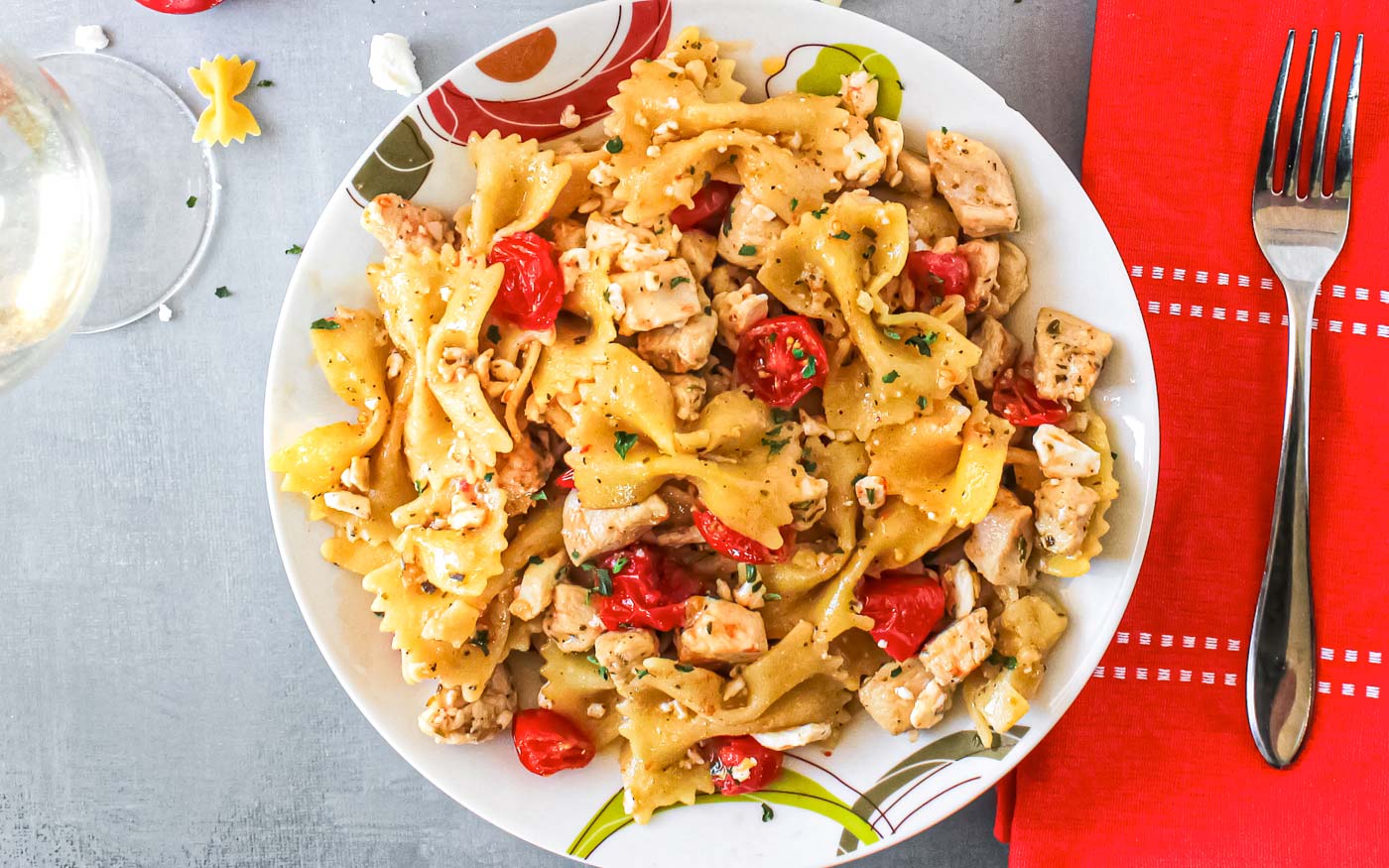 Plate of chicken white wine pasta featuring bowtie pasta, cherry tomatoes and feta cheese crumbles.