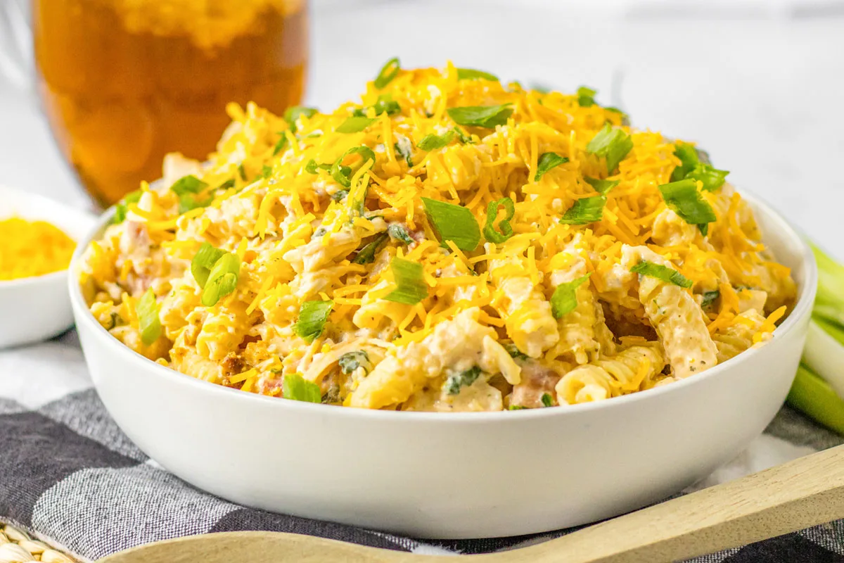 White bowl filled with crock pot chicken bacon ranch pasta topped with shredded cheddar cheese and green scallions.
